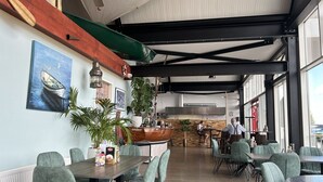 A restaurant with a wooden floor, green upholstered chairs, a counter with a wooden top, and a large window.