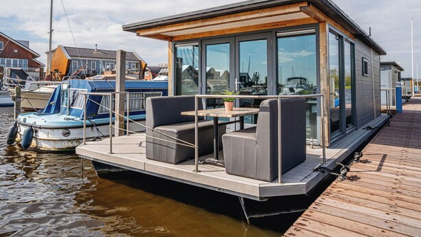 A floating house with a deck, seating area, and large windows.
