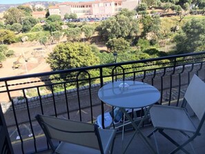 A balcony with a table and chairs, overlooking a construction site and a building with parked cars. - Residence Hoteliere En Aparte (Porto-Vecchio)