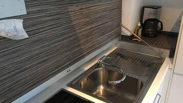 A compact kitchen with a stainless steel sink, a coffee maker, and a paper with a drawing on the wall.
