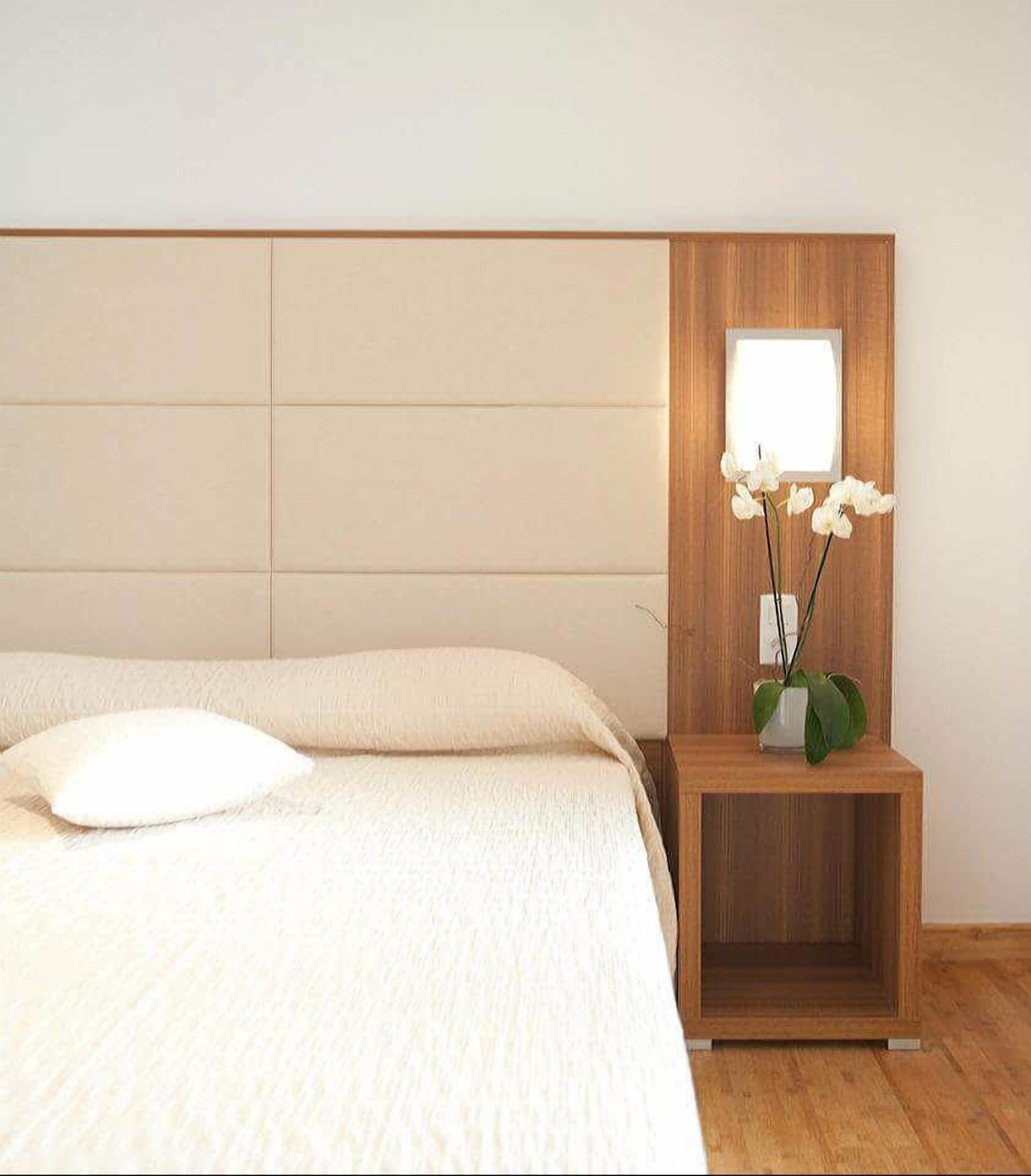 A bedroom with a bed, a nightstand with a vase of flowers, and a wooden headboard.