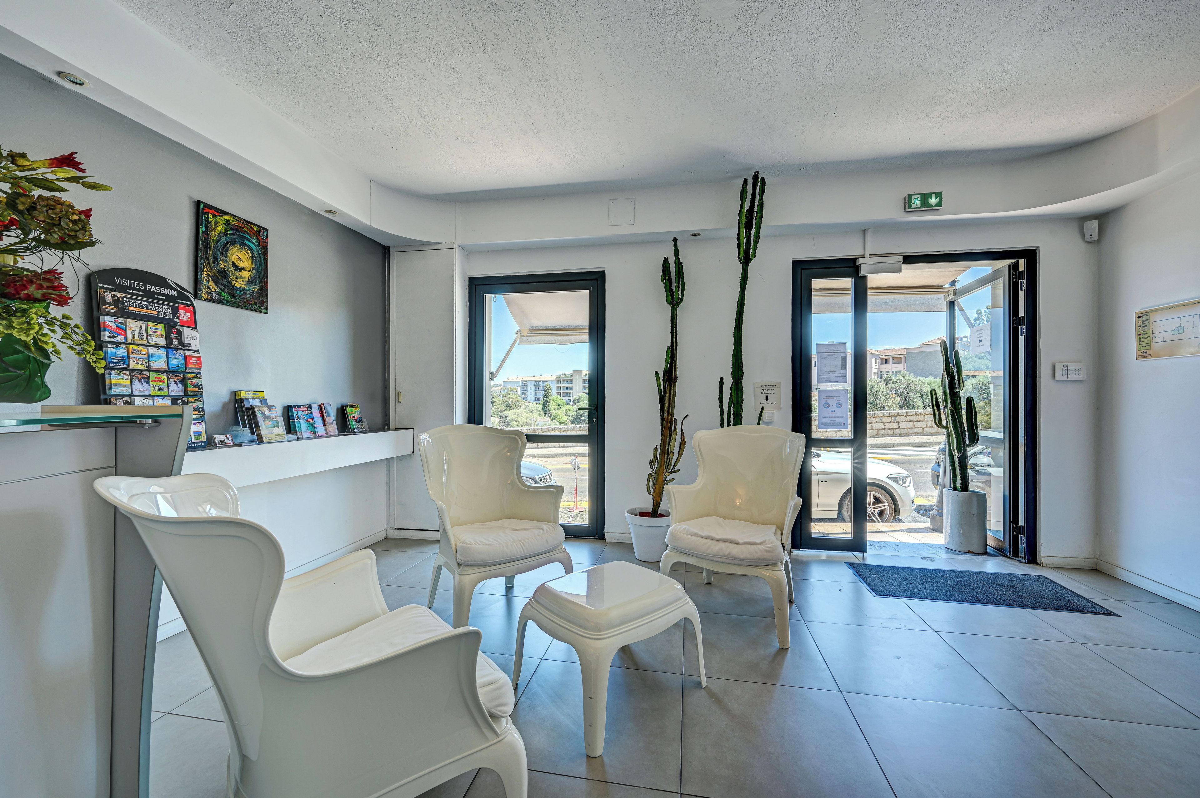 A reception area with a counter, two white chairs, a potted plant, and a view through the door.