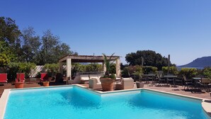 Zona de piscina con sillones de descanso y una pérgola, rodeada de vegetación y con vistas panorámicas.