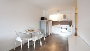 Una cocina moderna con armarios blancos, un refrigerador y un comedor con mesa y sillas de vidrio.