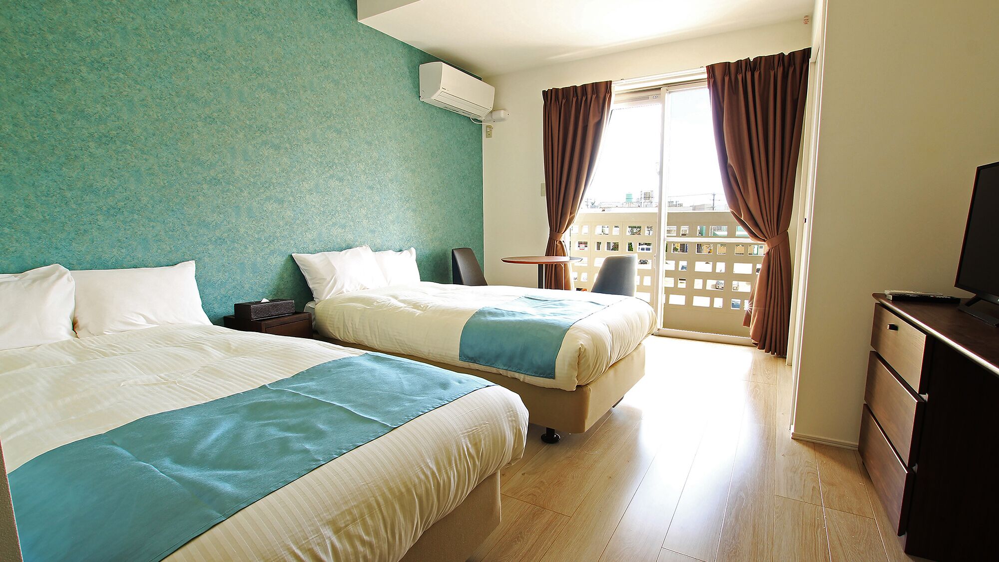 Une chambre d’hôtel avec deux lits, un bureau, une télévision et un balcon avec des rideaux.