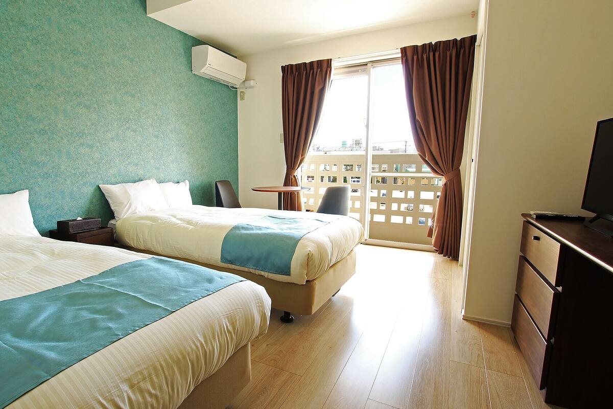 Une chambre d’hôtel avec deux lits, un bureau, une télévision et un balcon avec des rideaux.