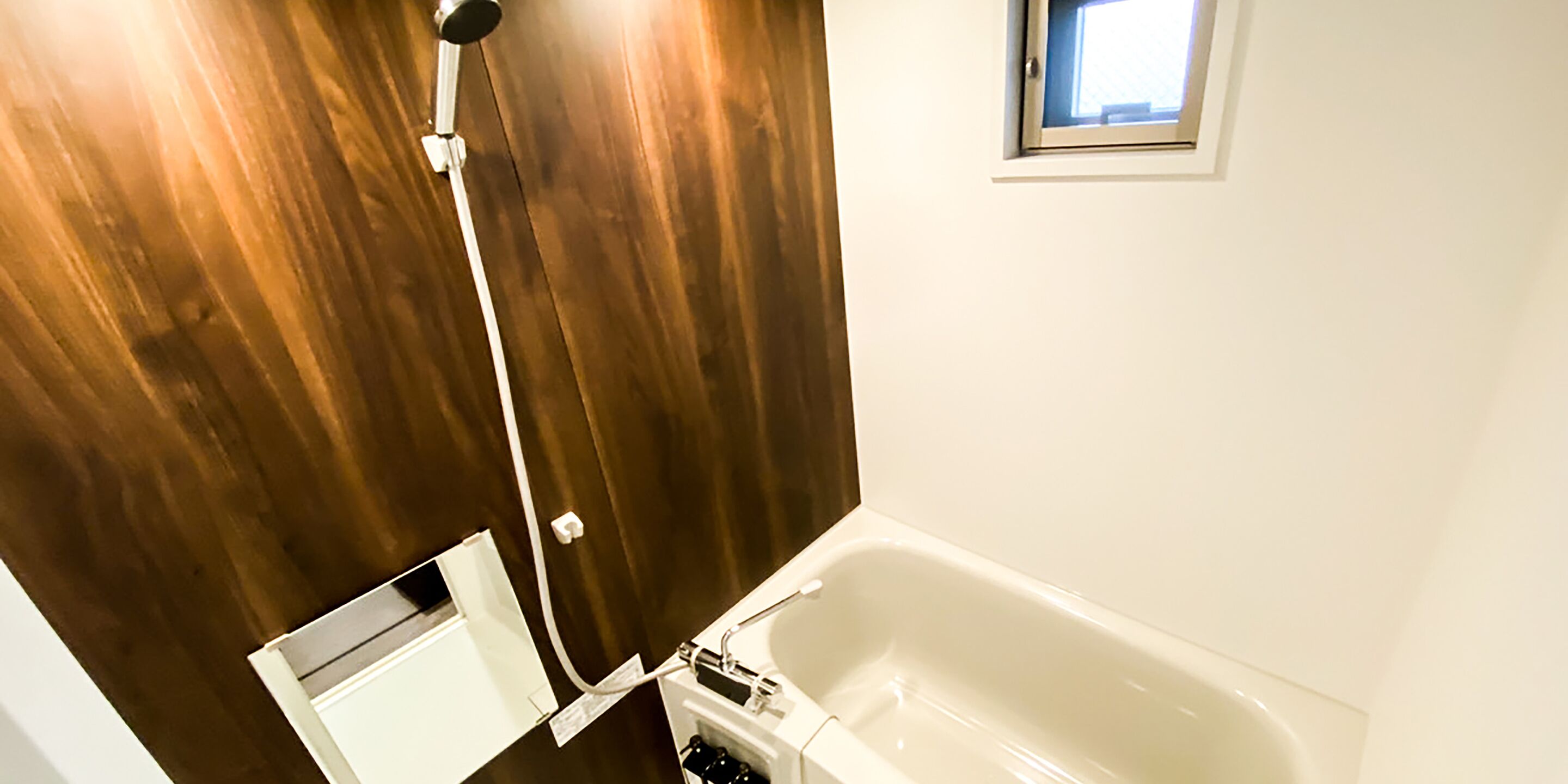 A bathroom with a wooden wall, a white bathtub, and a small window above the tub.
