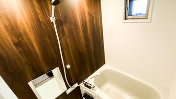 Un baño con pared de madera, una bañera blanca y una pequeña ventana sobre la bañera.