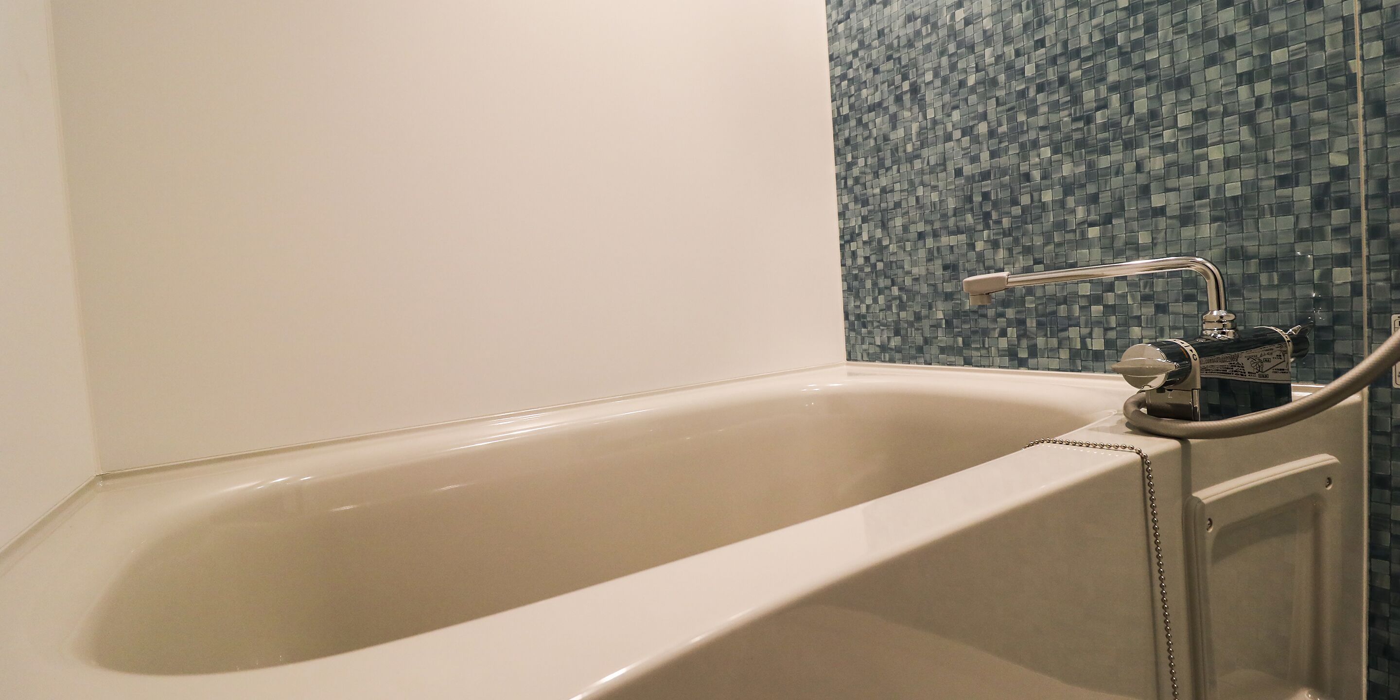 A bathtub with a modern faucet and a showerhead, adjacent to a tiled wall.