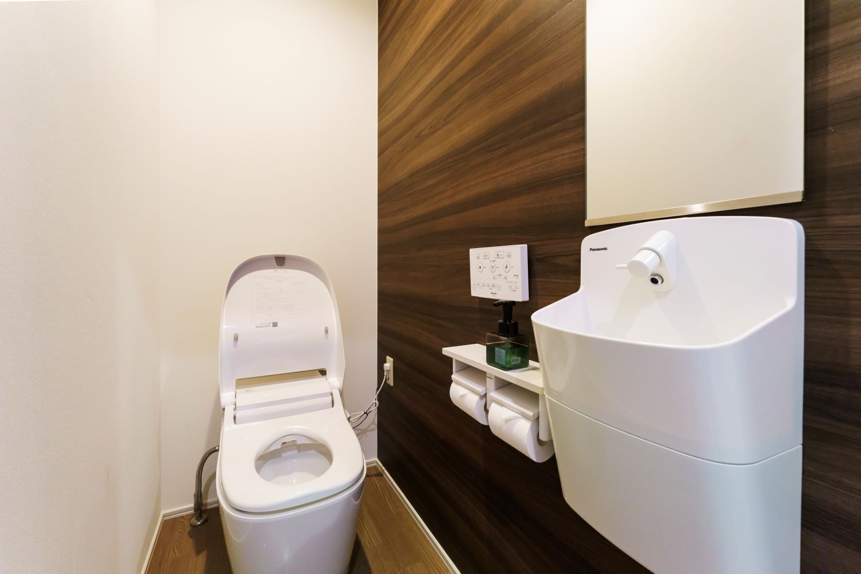 A modern bathroom with a white toilet, a wall-mounted bidet, and a wooden panel wall.