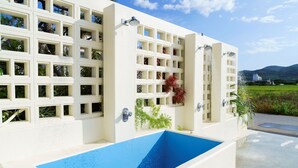 Un bâtiment moderne doté d’une grande piscine rectangulaire, de nombreux balcons ornés de plantes et offrant une vue dégagée sur le paysage environnant.