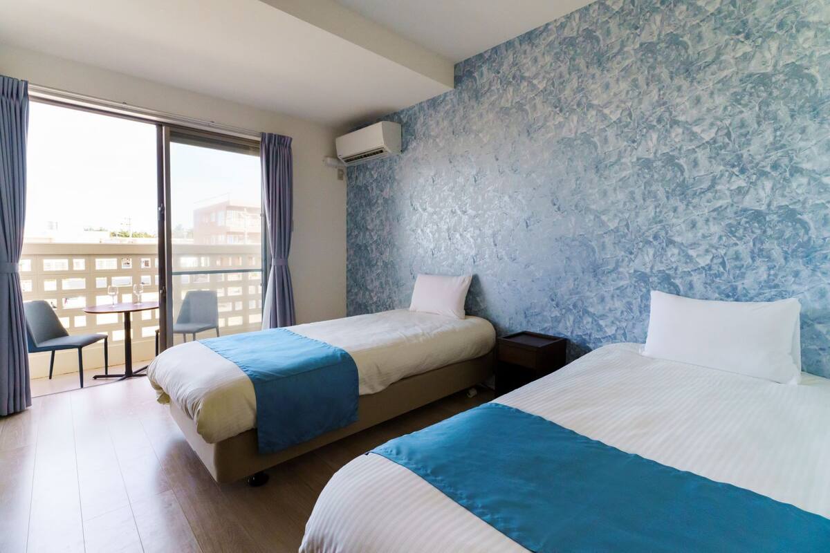Une chambre d’hôtel avec deux lits, un balcon avec des chaises et une grande fenêtre.