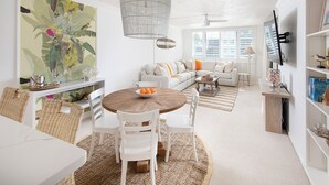 A modern living room with a round wooden table, white chairs, a sofa, and a large abstract painting. - The Cocohut Sanibel at Loggerhead Cay 🐚 Beachfront Condo with Pool & Pickleball (Sanibel)