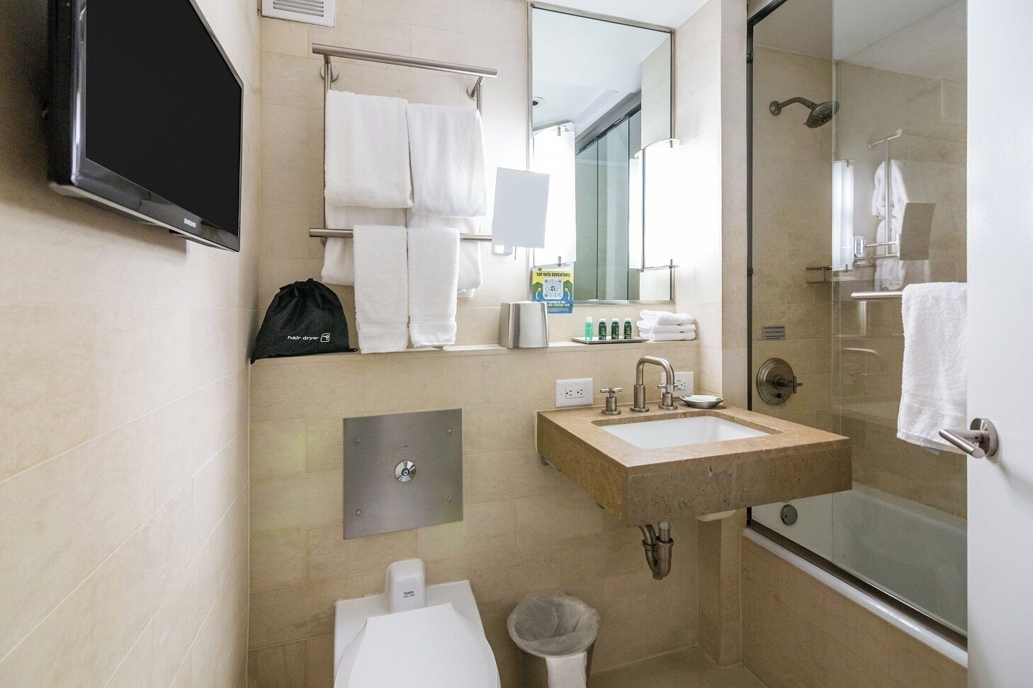 A modern bathroom with a sink, mirror, towel rack, and a hair dryer bag.