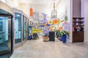 Moderni aula, jossa on seinämaalaus, oleskelualue ja vastaanottotiski.