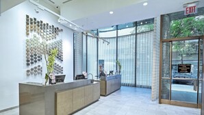 Zona d'entrada amb un disseny modern, que destaca una gran paret de mostres de rajoles, una recepció i una porta de vidre que dona a l'exterior.