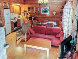 A cozy cabin interior with a wooden dining area, a red sofa, and a television.