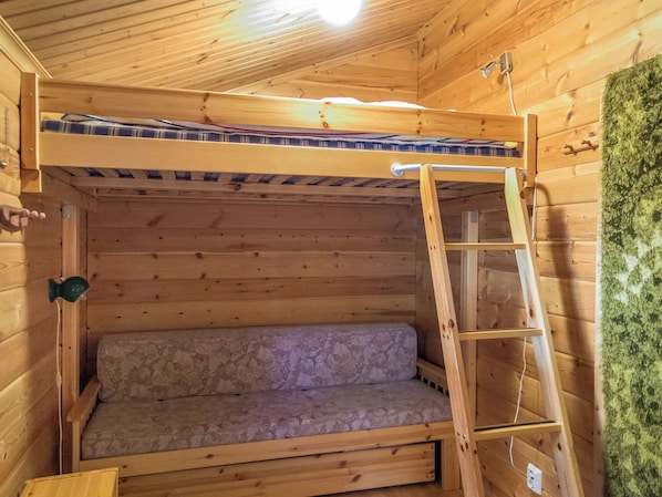 A wooden bunk bed with a ladder, a mattress, and a wall with a textured surface.