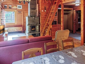 Een gezellig blokhutinterieur met een stenen openhaard, houten wanden, een eethoek en een trap.