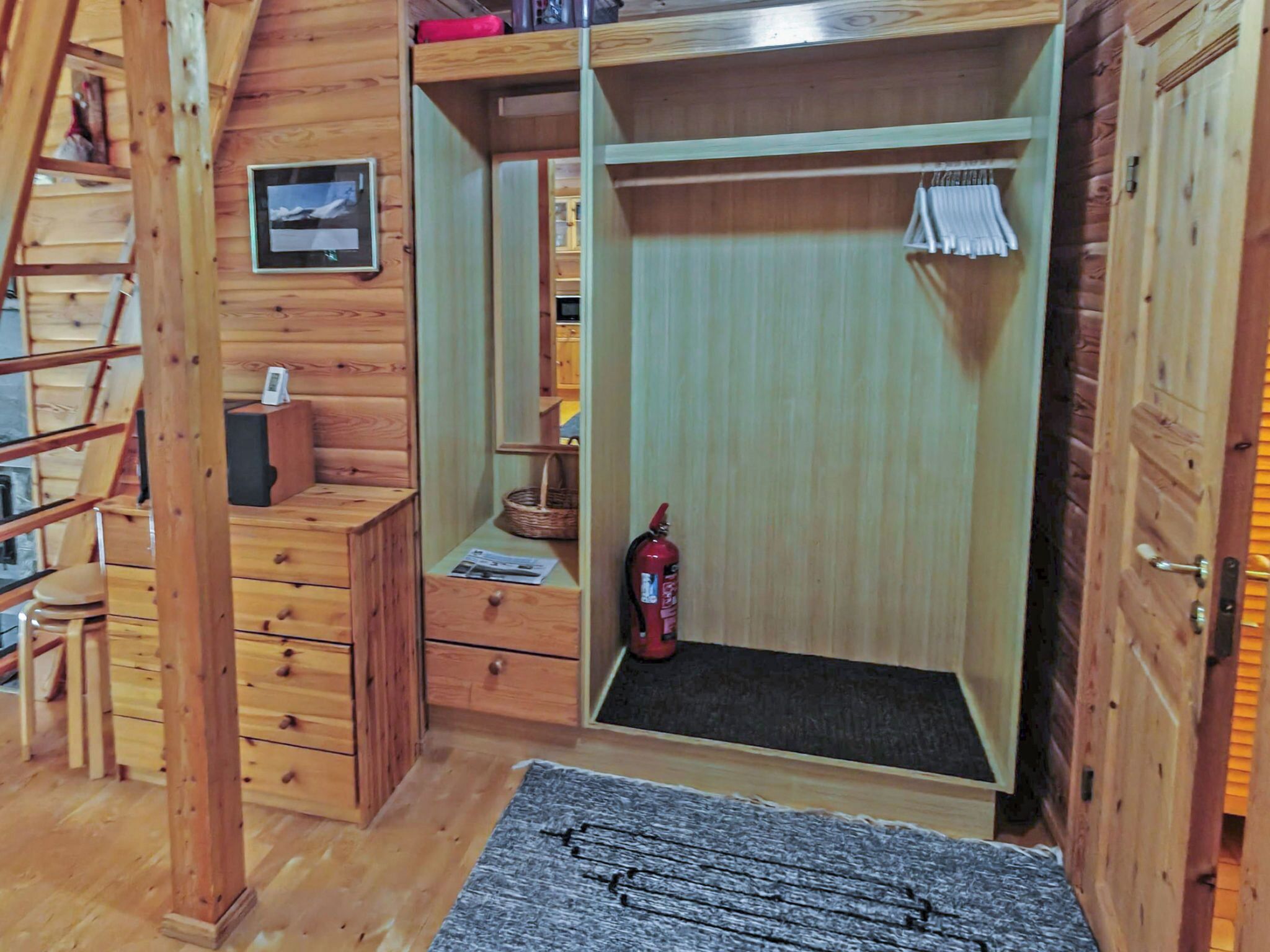 Interior de madera con cama tipo litera, un pequeño escritorio, un extintor y un cuadro en la pared.