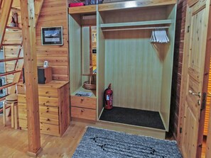A wooden interior with a loft bed, a small desk, a fire extinguisher, and a framed picture on the wall.