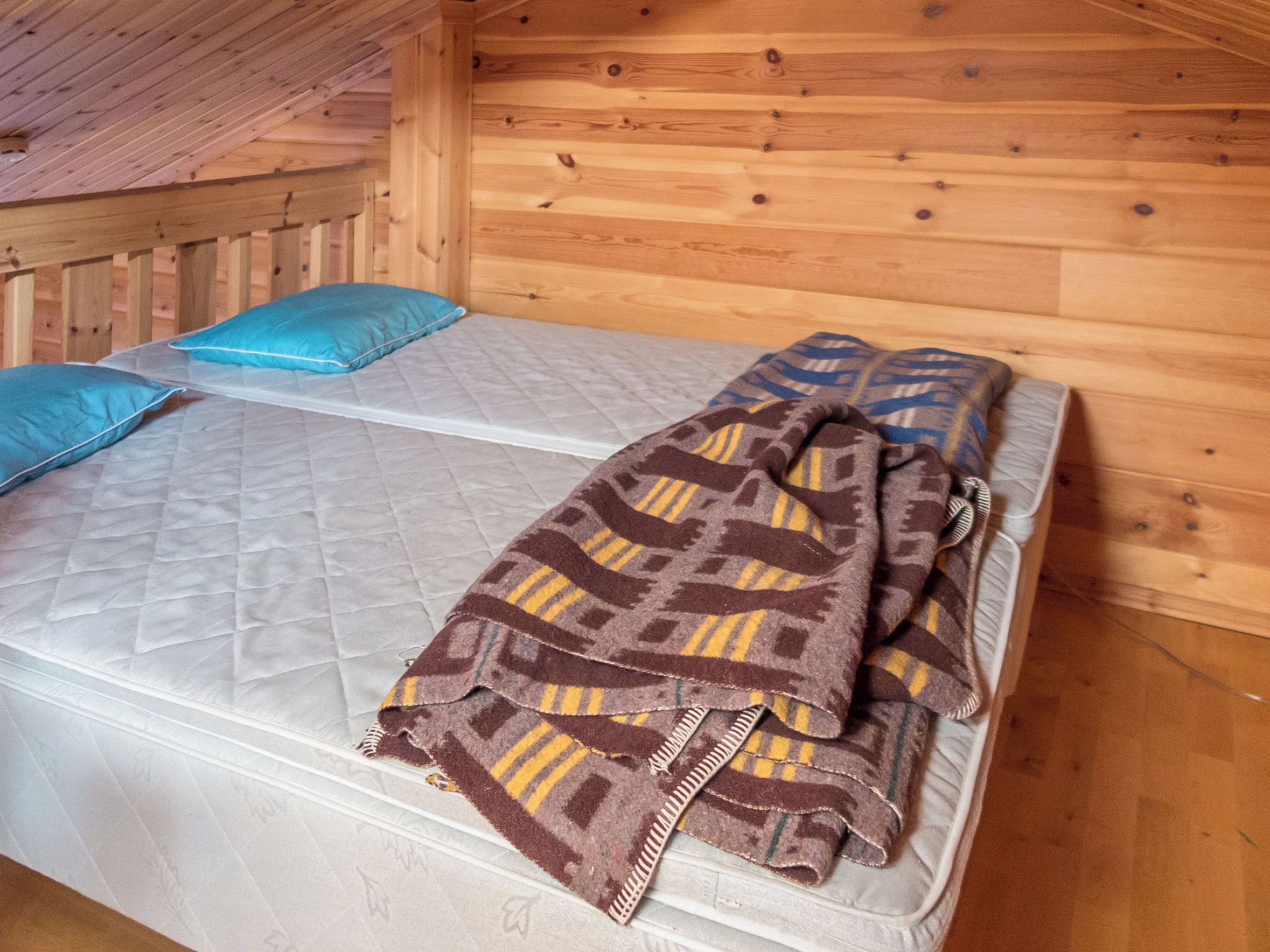 Un lit simple avec un matelas matelassé et une couverture à motifs, un oreiller bleu et une tête de lit en bois, dans une pièce aux murs en bois.