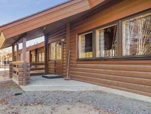 A wooden cabin with a covered porch, large windows, and a gravel driveway.