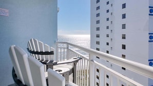 A balcony with white chairs and a table, overlooking a building and a body of water. - HS-1017 Ocean View Retreat on the 10th Floor in Myrtle Beach, Sleeps 6 (Myrtle Beach)