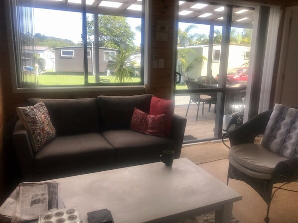 Un salon avec un canapé, une table basse et un fauteuil. Il y a une fenêtre donnant sur une maison et une voiture.