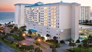 A multi-story hotel with a central courtyard, surrounded by palm trees and a parking area.