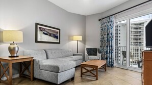 A living room with a grey sofa, two side tables, a floor lamp, a television, and a patterned curtain.