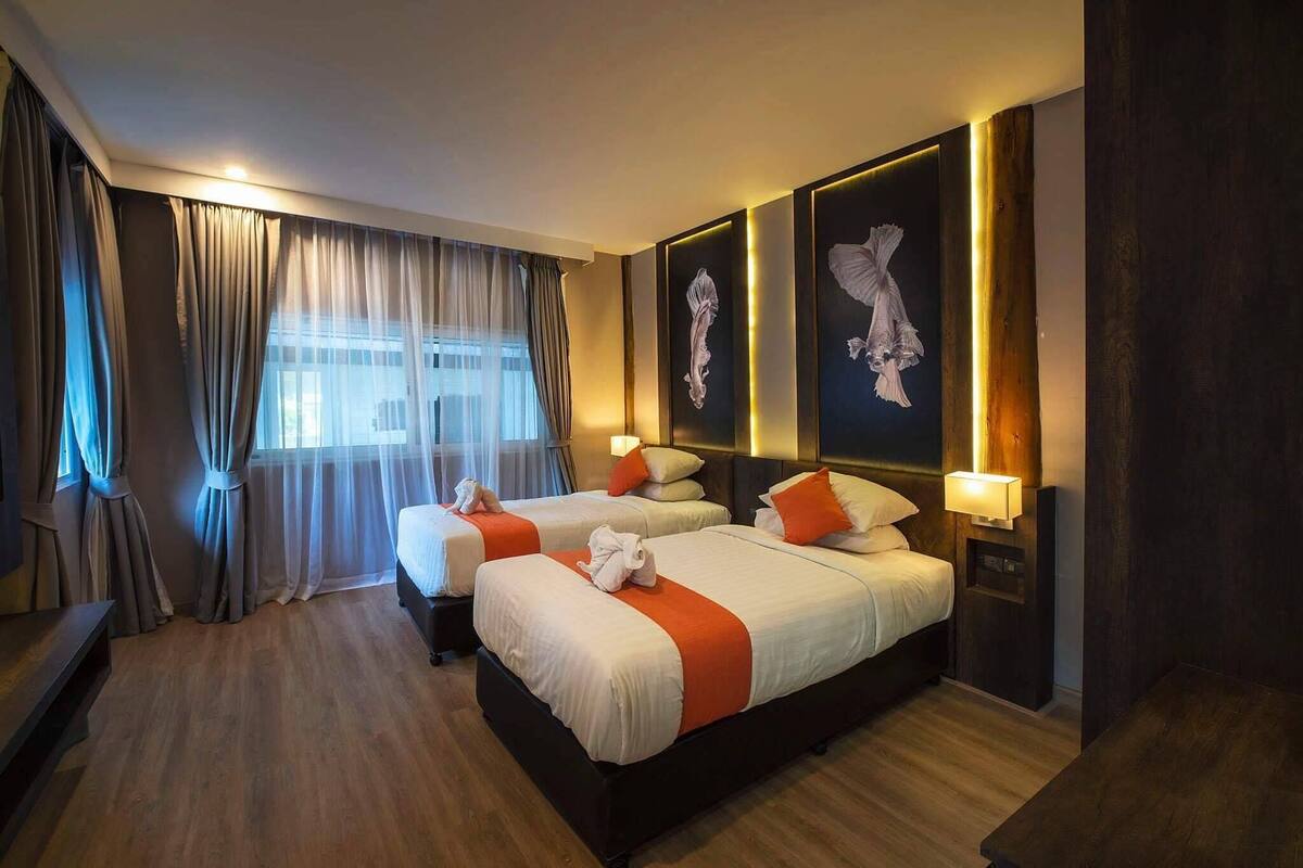 Habitación de hotel con dos camas, un ventanal con cortinas, lámparas de pared y obras de arte.