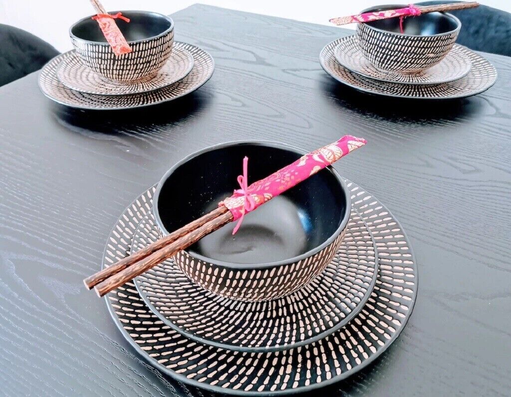 A table with three black bowls and chopsticks on a black tablecloth.