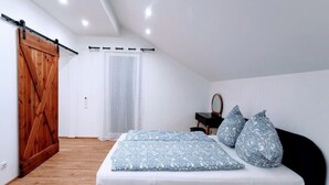 A bedroom with a bed, a wooden door, a chair, and a mirror. - Charming Vacation Home “Ludwig der XVI” with Wi-Fi, Terrace & Garden (Schwandorf)