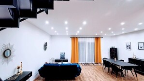 A modern living room with a blue sofa, a dining table with chairs, a black TV stand, and a decorative mirror. - Charming Vacation Home “Ludwig der XVI” with Wi-Fi, Terrace & Garden (Schwandorf)