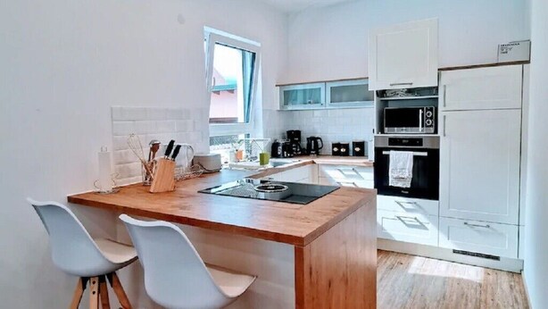 A modern kitchen with a central island, white cabinetry, and a wooden floor. - Charming Vacation Home “Ludwig der XVI  ” with Wi-Fi, Terrace & Garden (Schwandorf)