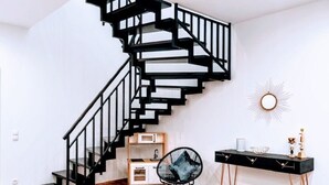 A modern interior with a spiral staircase, a black chair, a desk with a vase, and a sunburst wall decoration. - Charming Vacation Home “Ludwig der XVI” with Wi-Fi, Terrace & Garden (Schwandorf)