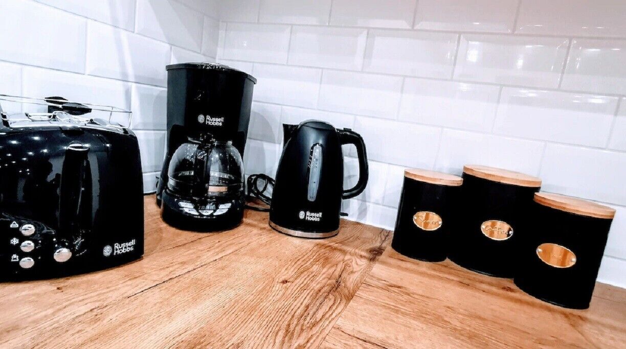 Una cocina con cafetera, hervidor y taburetes de madera.