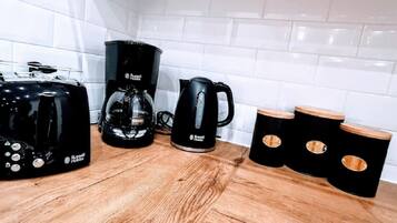 Una cocina con cafetera, hervidor y taburetes de madera.
