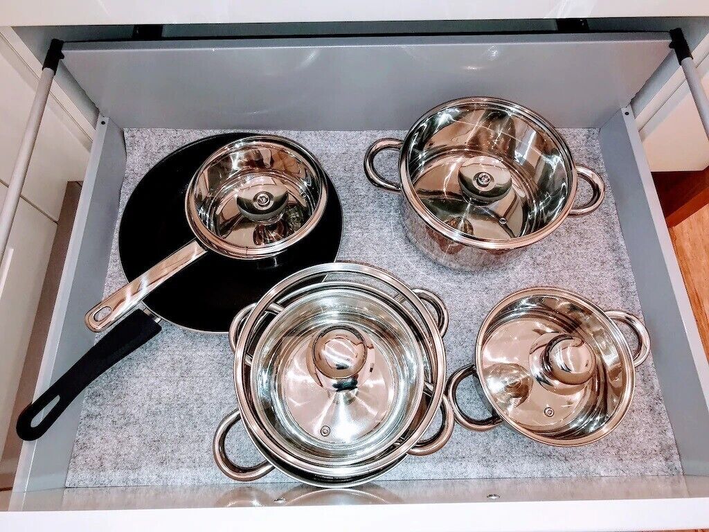 Un cajón de cocina con cuatro ollas de acero inoxidable y una sartén.