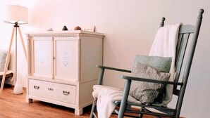 Habitació amb una cadira d'oscil·lació, un armari blanc i una làmpada de peu.