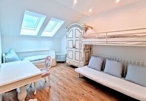Una habitación con una cama litera, un sofá, una mesa y una silla. Hay tragaluces y un armario.