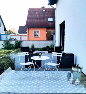 Un patio con una mesa y sillas, un jardín pequeño y una casa al fondo.