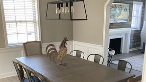 Une salle à manger avec une table en bois, des chaises en métal et un coq décoratif en guise de centre de table.