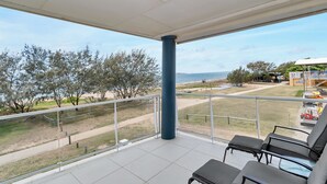 En balkon med udsigt over stranden, en blå søjle og en række sorte stole.