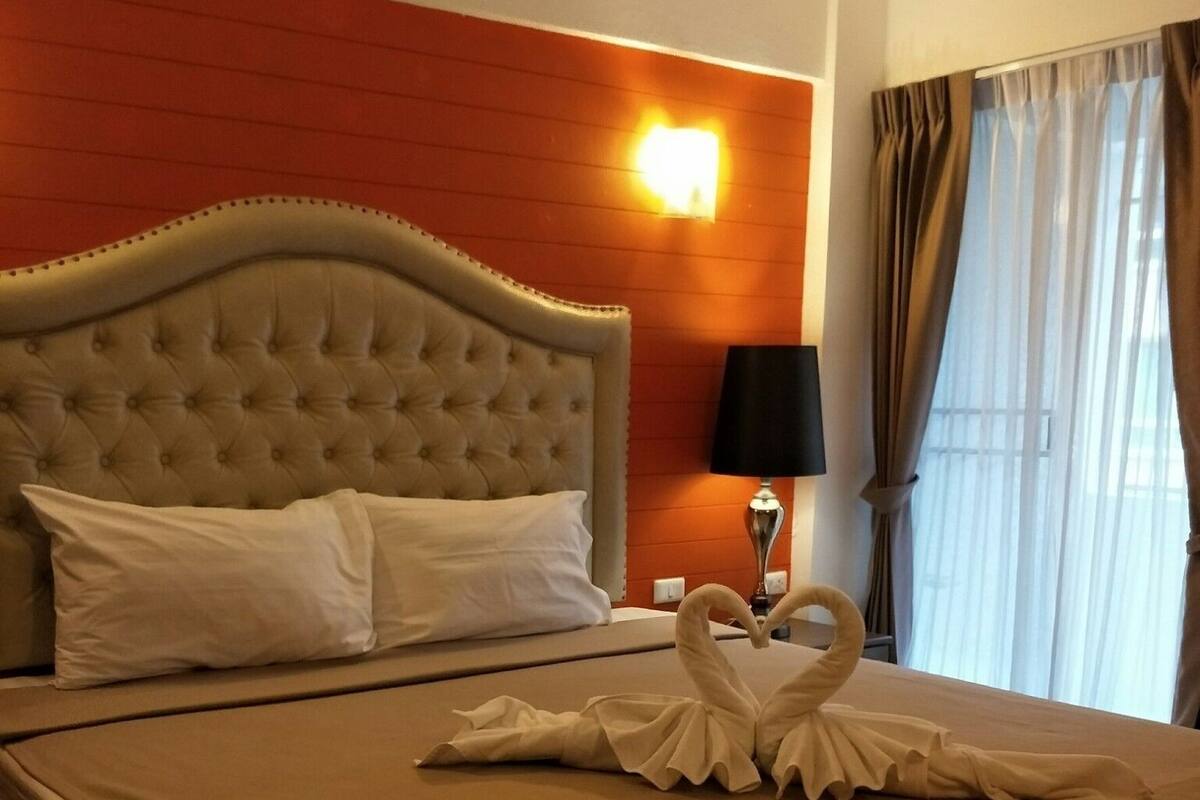 A hotel room with a large bed, a headboard, a nightstand, a lamp, and a window with curtains.