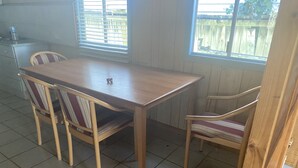 A dining area with a wooden table and four chairs, a tiled floor, and windows with blinds. - Camping with a Roof, bathroom and Kitchen (Palm Beach)
