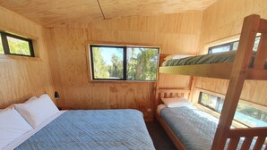 A wooden cabin room with two bunk beds, a large bed, and a window providing a view of trees. - Treescapes (Punakaiki)