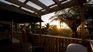 A covered outdoor area with a wooden deck, a table with chairs, and a grill. - Treescapes (Punakaiki)