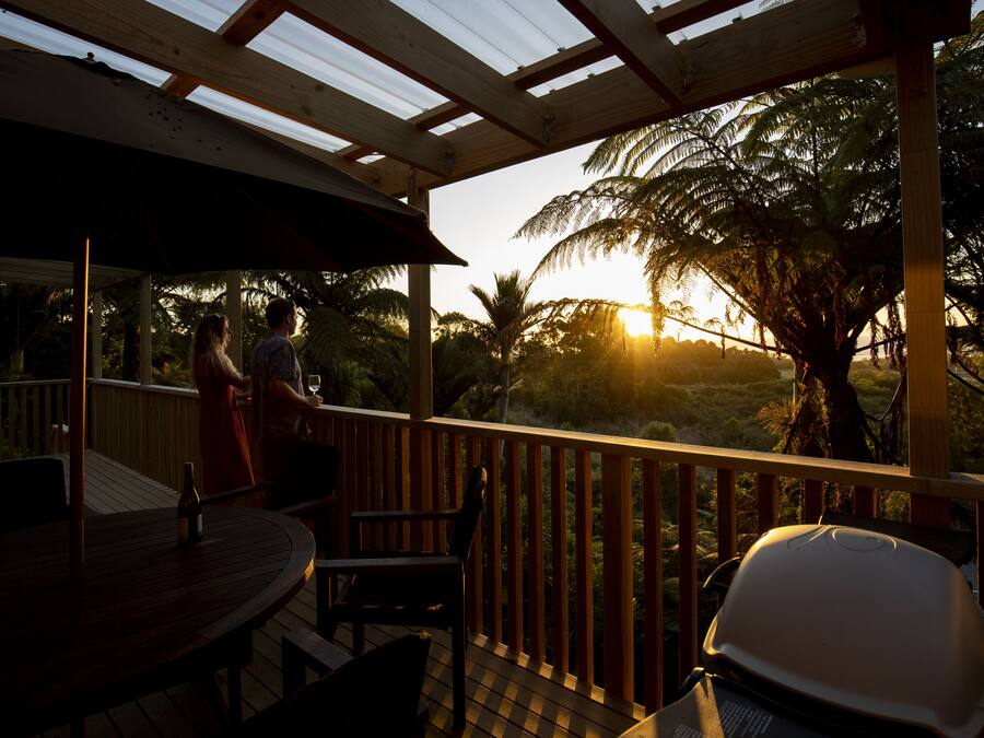 Um espaço coberto ao ar livre com deck de madeira, mesa, cadeiras e churrasqueira.